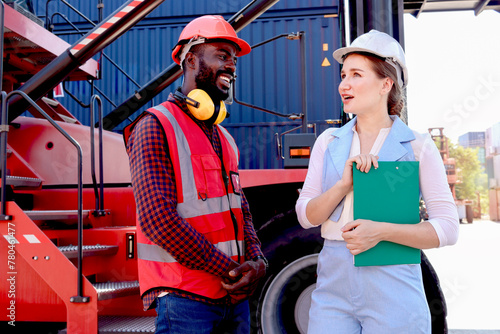 Two workers with safety helmet at logistic shipping cargo containers yard. African American engineer man discuss results with his beautiful woman boss who holds document folder at workplace.