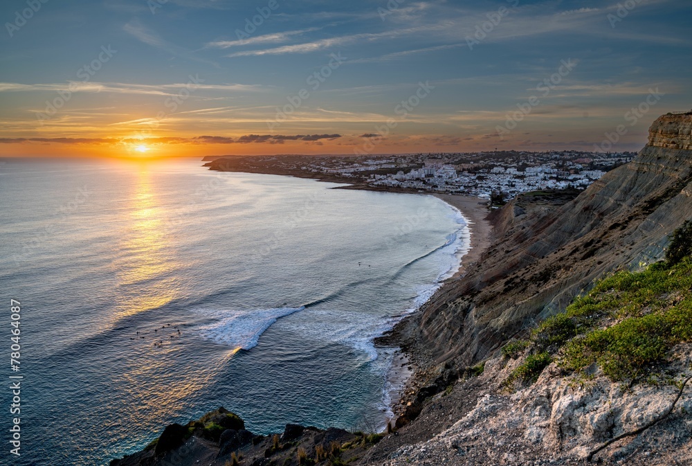 Scene of the ocean with the rocky beach illuminated by sun rays at sunset in Praia da Luz, Portugal Scene of the ocean with the rocky beach illuminated by sun rays at sunset in Praia da Luz, Portugal