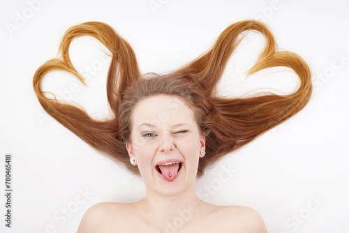 Young woman with hair forming heart shape and winking while sticking out tongue © Axel Bueckert