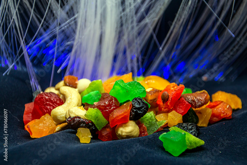 Beautiful multi-colored candies and nuts on a black background with glowing blue garlands in the background, close-up 