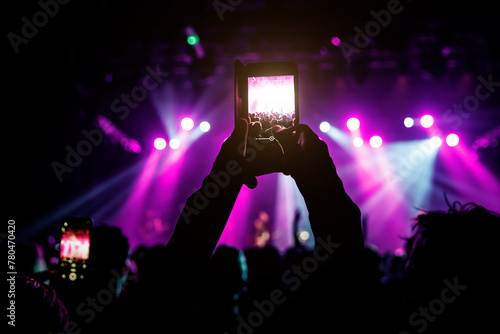 A hand holds a smartphone, recording a lively event illuminated by colorful lights