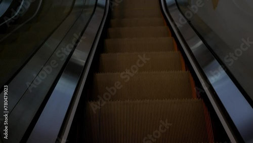 Close-up from above shows the legs of a human, a pair in the shoes sneakers of a traveler using a moving down escalator in the airport terminal. Top view of the legs on the escalator in the mall. photo
