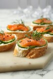Tasty canapes with salmon, cucumber and cream cheese on white marble table, closeup