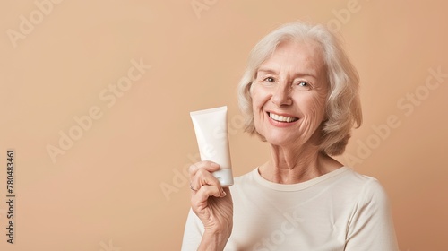 Donna anziana sorridente, mostra un tubetto di crema per il viso photo