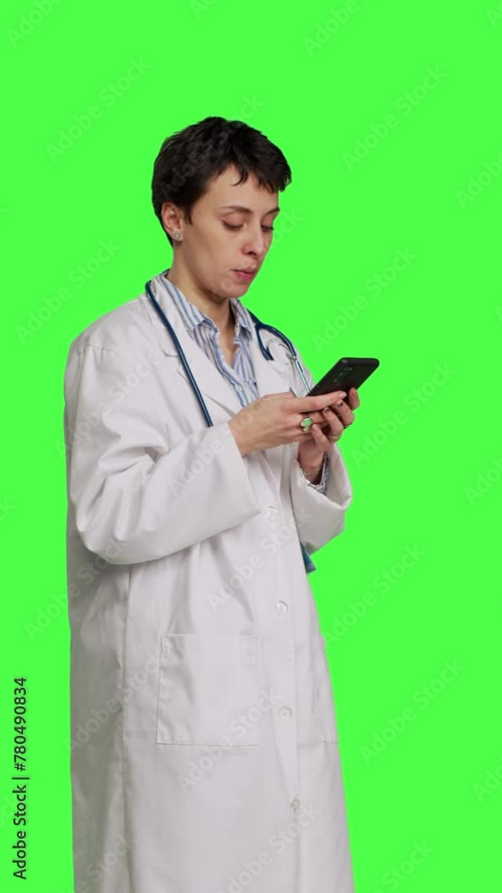 Side view Physician navigating on social media apps to text people, stands against greenscreen backdrop. Medic in white coat browsing websites online, making checkup appointments. Camera B. Side view Physician navigating on social media apps to text people, stands against greenscreen backdrop. Medic in white coat browsing websites online, making checkup appointments. Camera B.