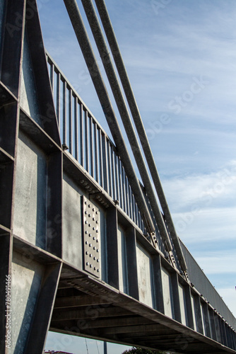 Close-up view of the steel structure of a modern bridge. Close-up of metal fence on the street. Detail of a steel bridge with blue sky in the background.