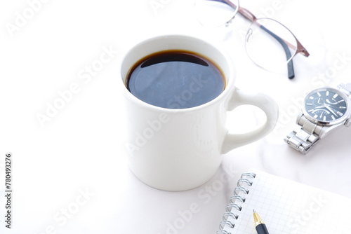 コーヒーを飲みながら、リング式のメモ帳とペンでデスクワークをしているイメージ 