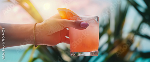 Close up of woman's hand holding a paloma grapefruit cocktail at sunset on beach paradise vacation photo