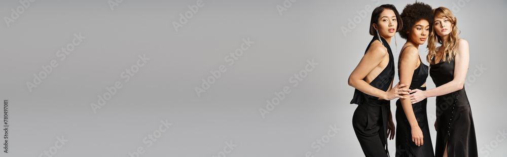 A diverse group of three women standing elegantly together against a grey studio background. A diverse group of three women standing elegantly together against a grey studio background.