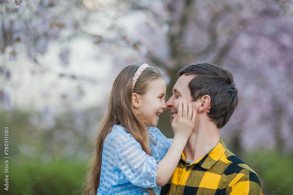 Father's Day Cute little blue-eyed girl with her smiling dad in blossoming sakura garden. Warm bright spring.