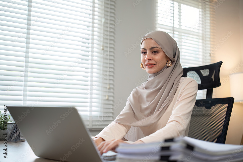 Muslim businesswoman working using laptop and taking notes on documents In the modern office Muslim businesswoman working using laptop and taking notes on documents In the modern office