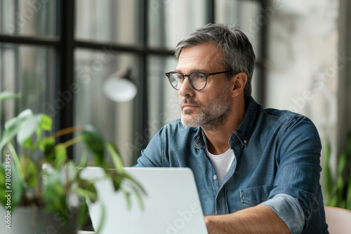 Side view of mid aged ambitious male entrepreneur using laptop computer sitting in modern office photo