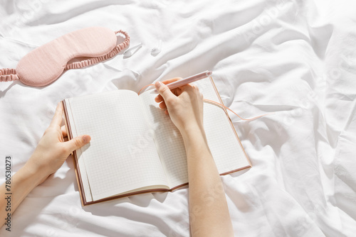 Woman takes notes or makes plan, day results on blank white page of paper in notebook or diary, holds notepad and pen in hands,  top view, time for yourself morning or evening before sleep