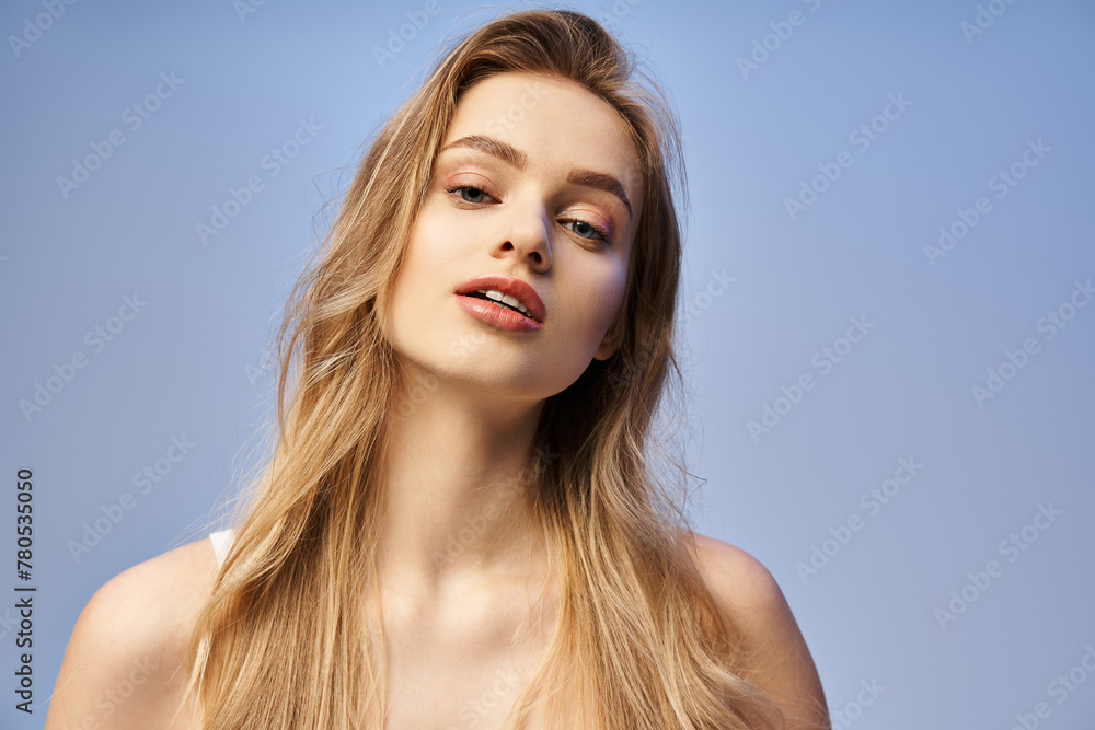 A young woman with long blonde hair stands gracefully in front of a vibrant blue sky backdrop. A young woman with long blonde hair stands gracefully in front of a vibrant blue sky backdrop.