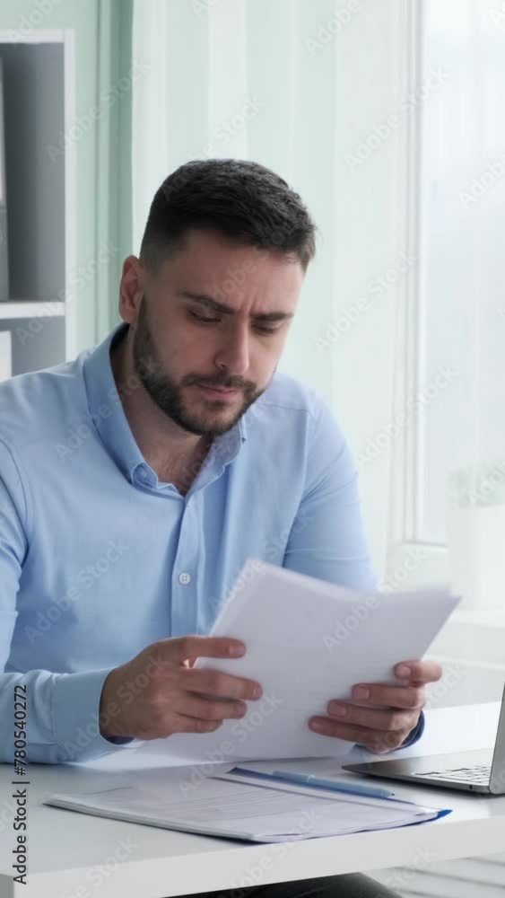 Contemplative Caucasian businessman sitting at desk, doing paperwork in office. Engaged in business research and accounting, reading information in documents. Vertical video. Contemplative Caucasian businessman sitting at desk, doing paperwork in office. Engaged in business research and accounting, reading information in documents. Vertical video.