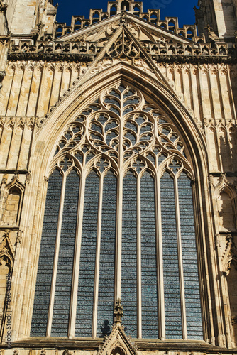 Gothic architecture detail of a cathedral window with intricate tracery and stained glass, set against a clear blue sky in York, North Yorkshire, England.