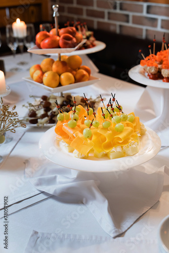 Cheese canapés with grapes, fruit plates in the background.