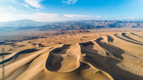 The first light of sunrise casts golden hues over the sweeping sand dunes of a vast and tranquil desert landscape. Aerial View of Majestic Desert Dunes at Sunrise  