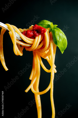 fork with Italian pasta spaghetti noodles tomato and basil macro close up on black background 