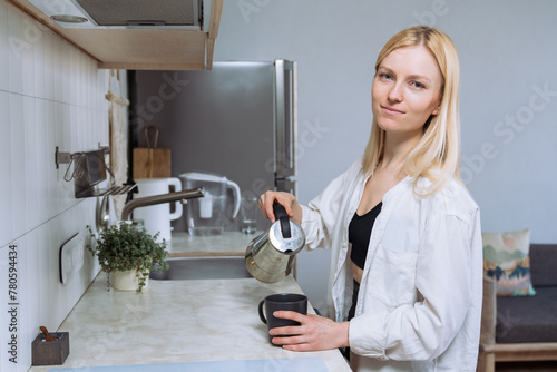 A young woman in a white shirt pours freshly brewed coffee into a cup.