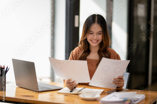 A focused businesswoman reviews documents at her desk with laptop and coffee