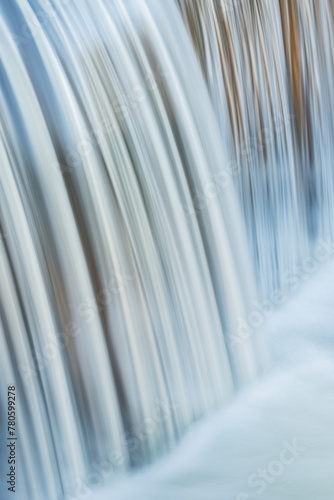 Portage Creek Cascade captured with motion blur and illuminated by reflected color from sunlit trees at sunrise and blue sky overhead  Michigan  USA