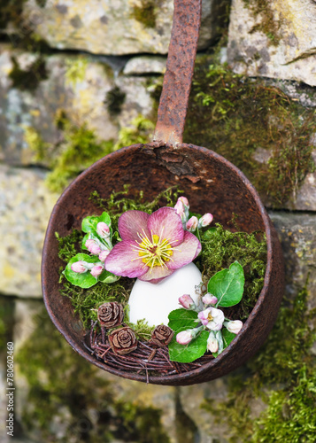 Beautiful easter floristic arrangement with Christmas rose flower apple blossoms  in an egg shell vase hanging on rusted soup ladle. Garden decoration or floristic concept 