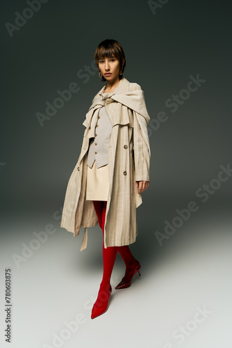 A stylish young woman in a trench coat showcases her unique style with eye-catching red tights in a studio setting.