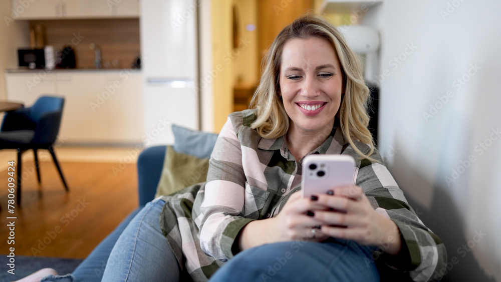 Mid adult woman sitting on the sofa and using smartphone Mid adult woman sitting on the sofa and using smartphone