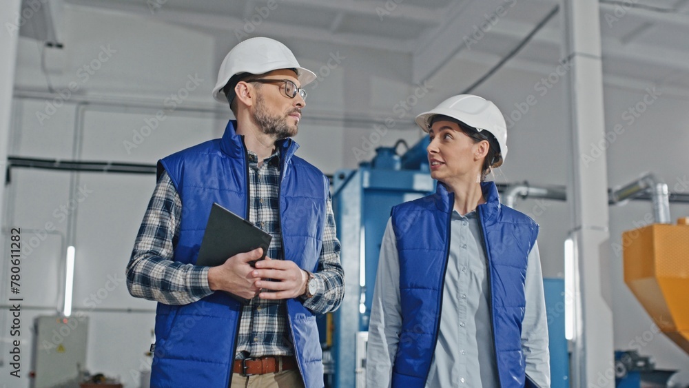Camera view of two Caucasian workers actively talking with each other while walking on large storage or industrial factory. Handsome man telling something important while young woman disagreeing. Camera view of two Caucasian workers actively talking with each other while walking on large storage or industrial factory. Handsome man telling something important while young woman disagreeing.