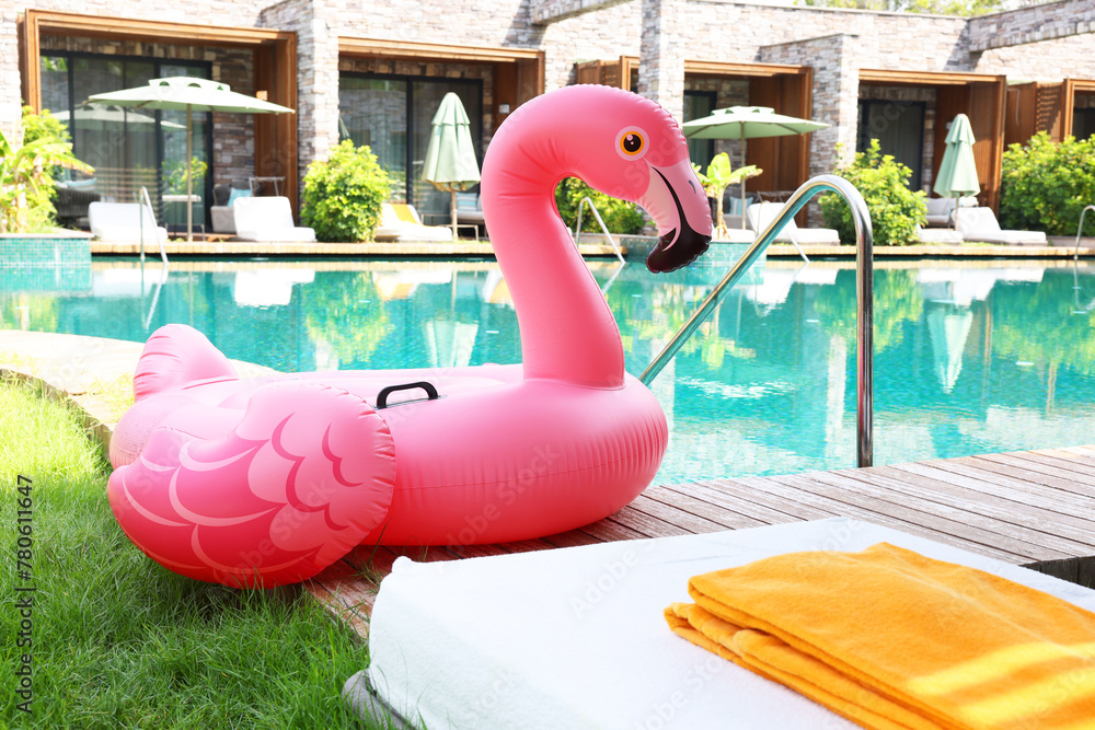 Fototapeta premium Float in shape of flamingo on wooden deck near swimming pool and sunbeds at luxury resort