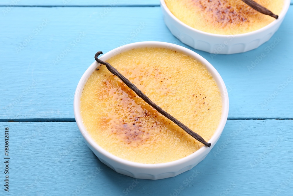 Delicious creme brulee in bowls and vanilla pods on light blue wooden table Delicious creme brulee in bowls and vanilla pods on light blue wooden table