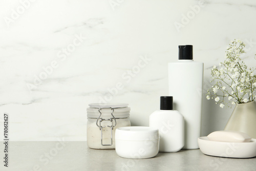 Bath accessories. Personal care products and gypsophila flowers in vase on gray table near white marble wall, space for text
