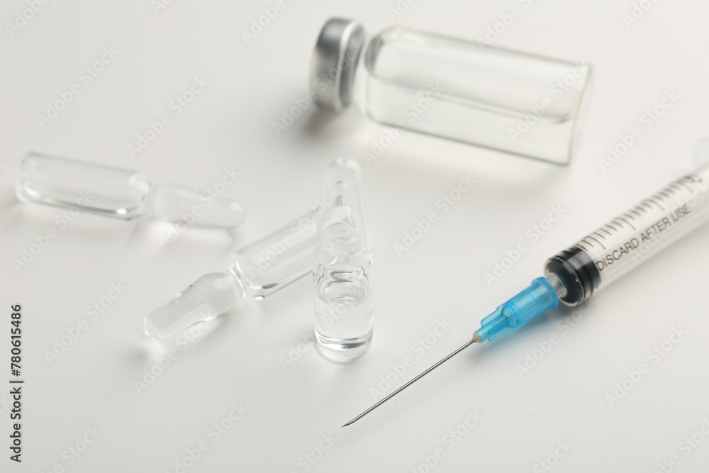 Glass ampoules with liquid and syringe on white background, closeup Glass ampoules with liquid and syringe on white background, closeup