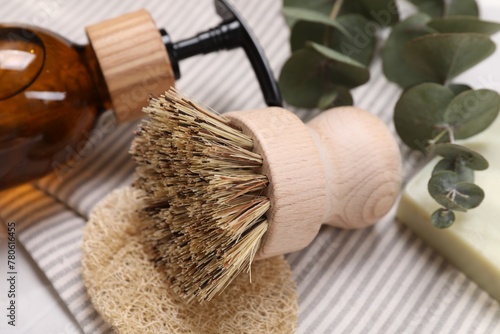 Cleaning brush, sponge, dispenser and eucalyptus leaves on table, closeup