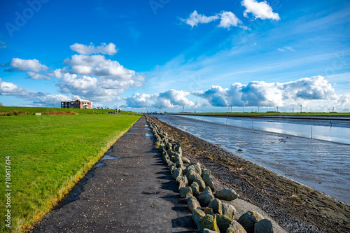 Waterfront of Husum with meadow on the left and sea on the right, beautiful clouds and wind turbines in the background, wide angle shot, Germany