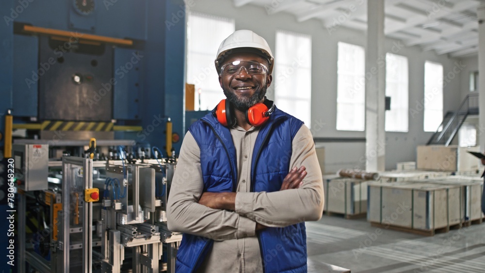Close-up portrait of professional joyful positive smiling African-American male worker. Man posing looking straight into camera. Specialist wearing white helmet blue vest at work.