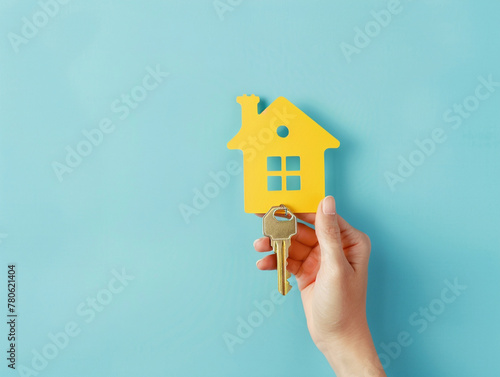 Hand holding yellow house symbol model with key on a light blue background.