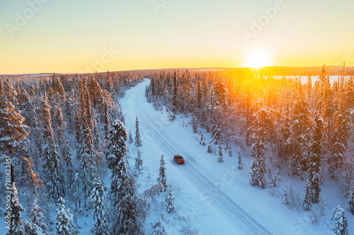 Car travels the icy and empty road crossing the boreal snowy forest at sunrise, Swedish Lapland, Sweden, Scandinavia photo