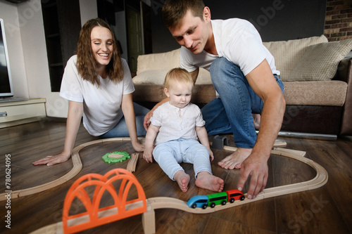 Child plays with wooden toy train and railroad in living room at home while sitting on floor with mom and dad,moving train. Developing imagination,natural,environmentally friendly toys,family together