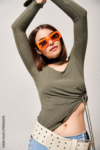 A young woman with brunette hair striking a pose in a green shirt and orange sunglasses.