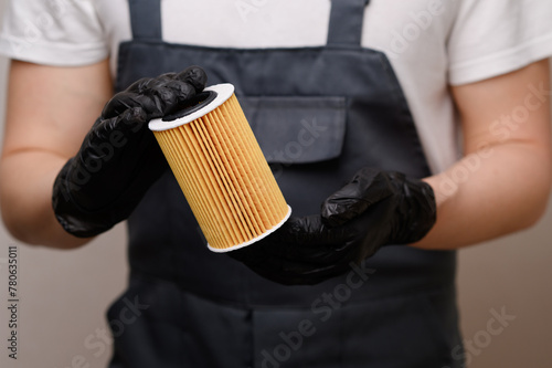 Auto repairman holds and rotates oil filter for diesel cars in black gloves, close-up. Concept of replacing auto parts, changing oil and car oil filter, car maintenance.