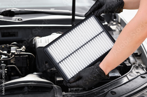 Replacing the air filter in a car. Auto mechanic in gray gloves holds an engine air filter against the engine compartment. Concept of maintenance, ecology, car care, auto parts