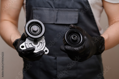 Auto mechanic holds in hands in black gloves tension roller with car serpentine belt tensioner and parasitic roller, close-up. Replacing auto parts, car maintenance, purchasing auto parts. photo
