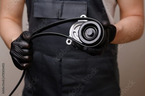 Auto parts salesman holds a tension pulley and a serpentine belt in his hands. Timely replacement of auto parts and vehicle maintenance. Sale of automotive products, provision of car repair services