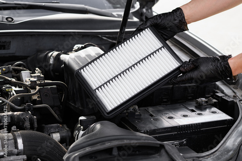 Car mechanic holds car air filter in hands near engine compartment, plans to replace old filter, close-up. Concept replacing auto parts, car maintenance, protection from allergens, dirt, soot