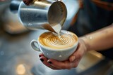A barista pouring steamed milk into a cup of coffee, focusing on the precise hand movements