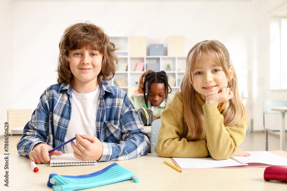Happy pupils sitting at desk in classroom while looking at camera. Education, learning concept Happy pupils sitting at desk in classroom while looking at camera. Education, learning concept