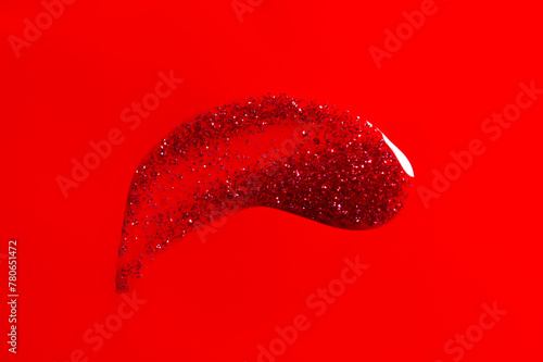 Red glitter nail polish UV gel smear. Nailpolish liquid smudge on red background, surface, red shellac UV gel brush, varnish, manicure concept. Manicure salon, shellac texture background. Top view