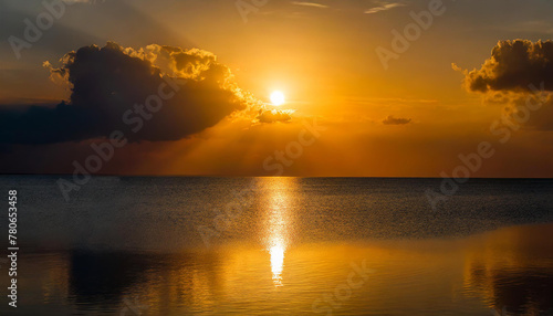 Red sunset over the sea. Large and round sun shining brightly against an orange sky with dark clouds. In front of it lies calm water reflecting © richard